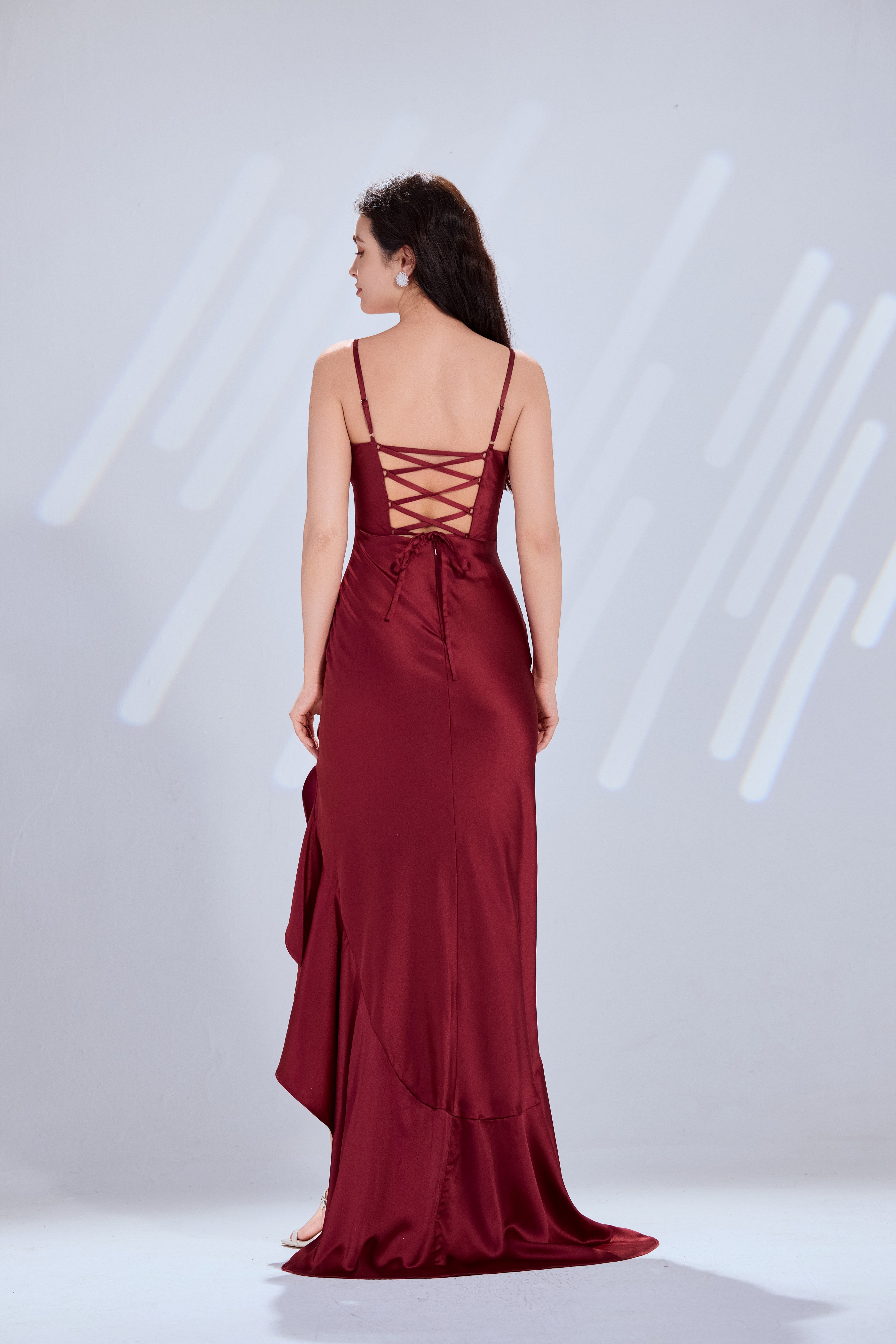 Wine satin prom gown from back view, with crisscross lace-up straps and long slit.