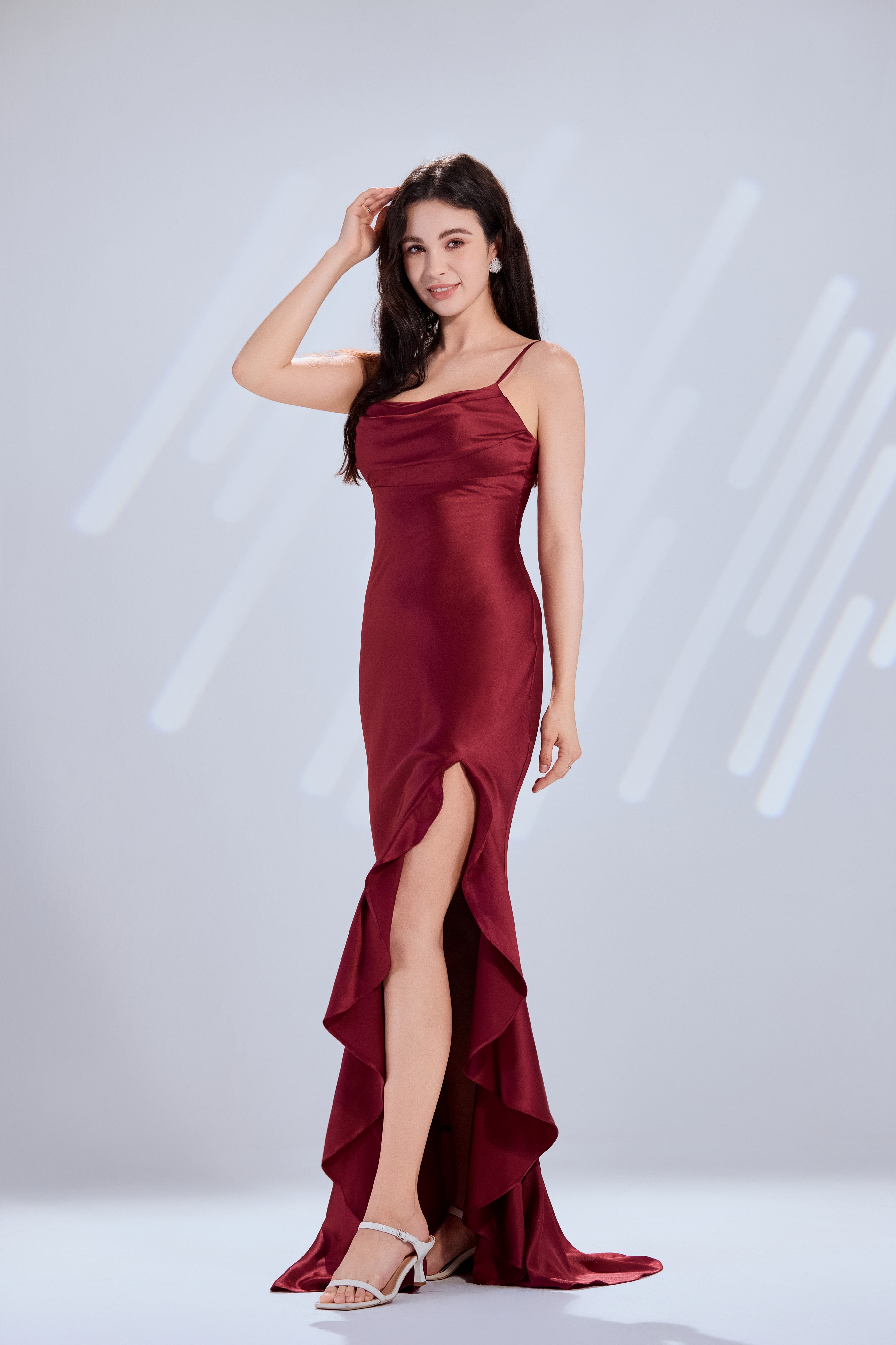 Wine satin prom gown on model, with spaghetti straps and layered ruffle hem over slit.