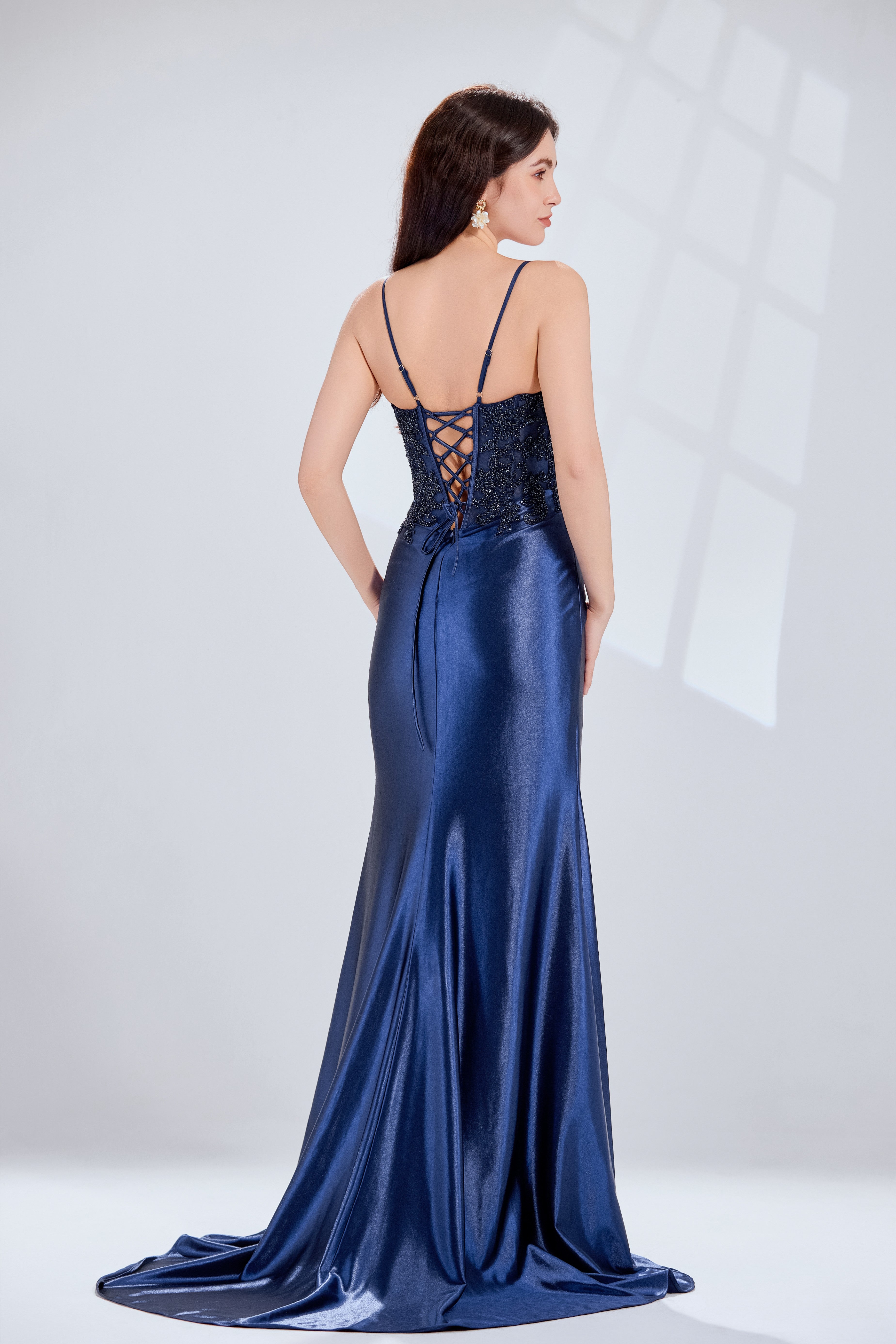 Front and back view of a navy blue evening gown featuring a sequined lace corset bodice with spaghetti straps and a draped satin skirt with a high slit.