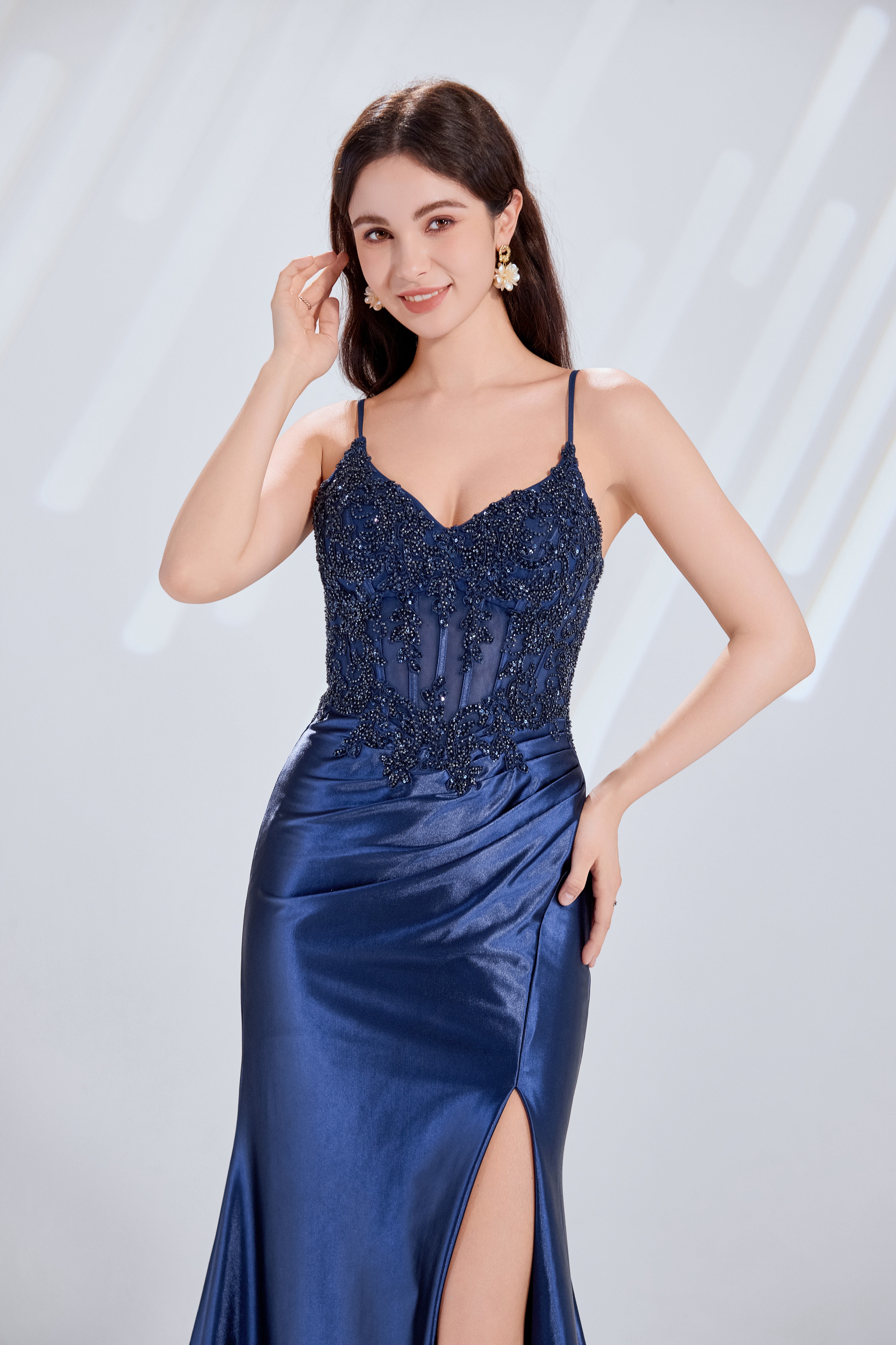 Front and back view of a navy blue evening gown featuring a sequined lace corset bodice with spaghetti straps and a draped satin skirt with a high slit.