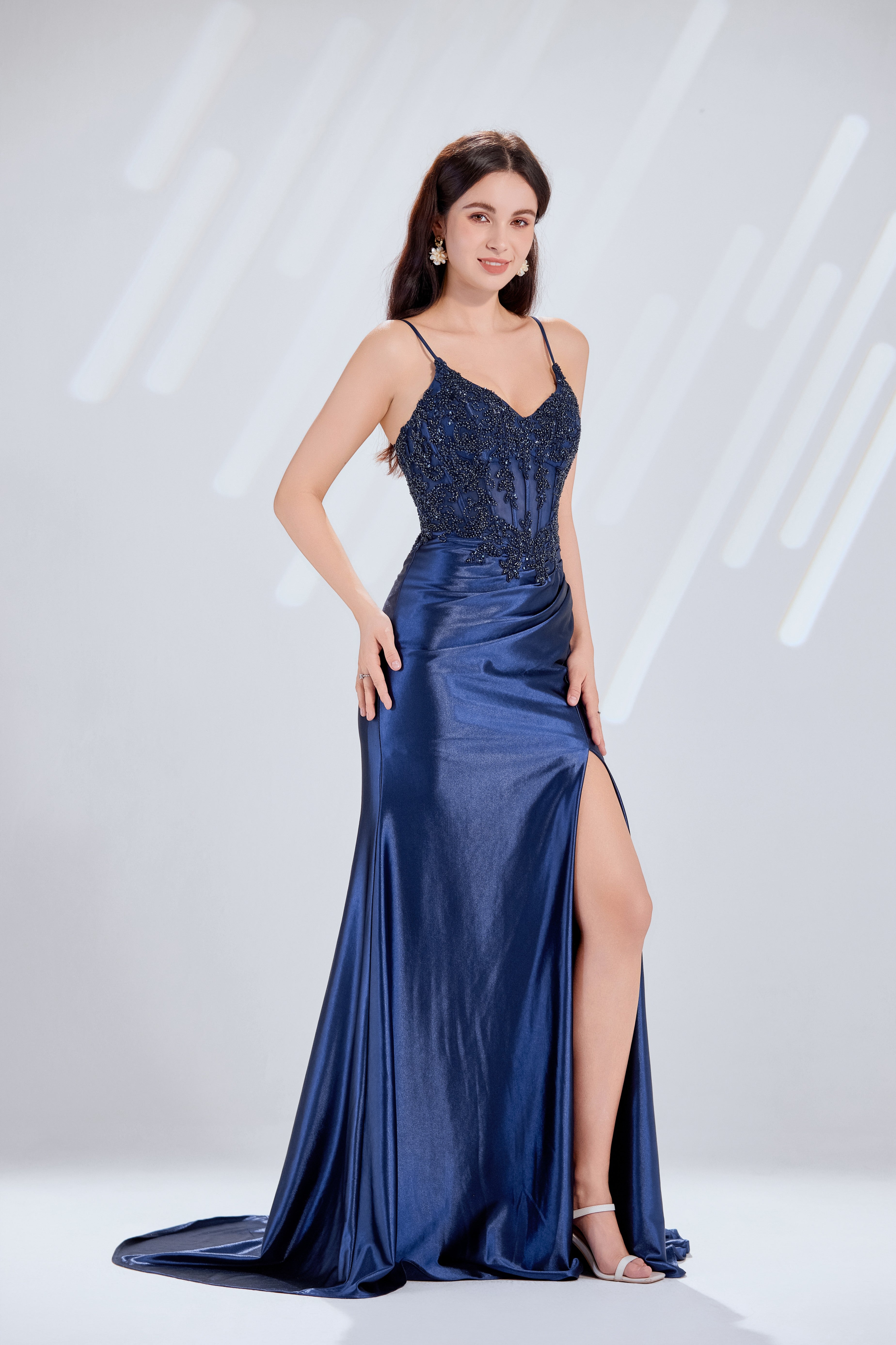 Front and back view of a navy blue evening gown featuring a sequined lace corset bodice with spaghetti straps and a draped satin skirt with a high slit.