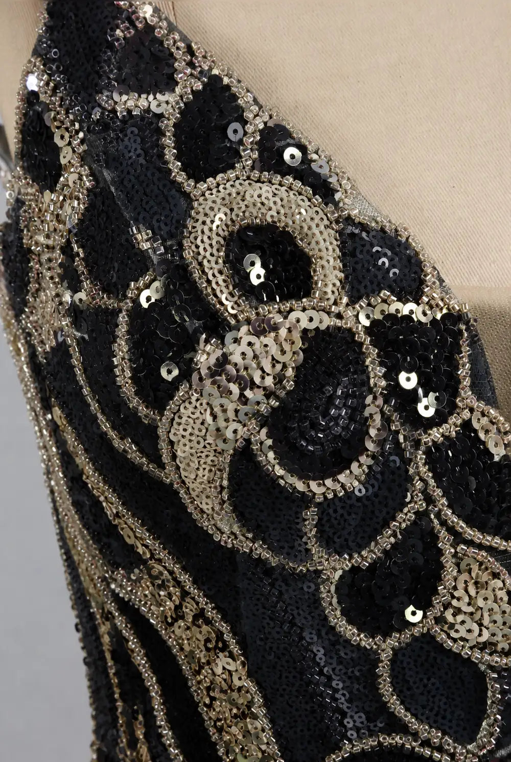 Black and gold sequin mini dress with ornate swirl and bead details, close-up