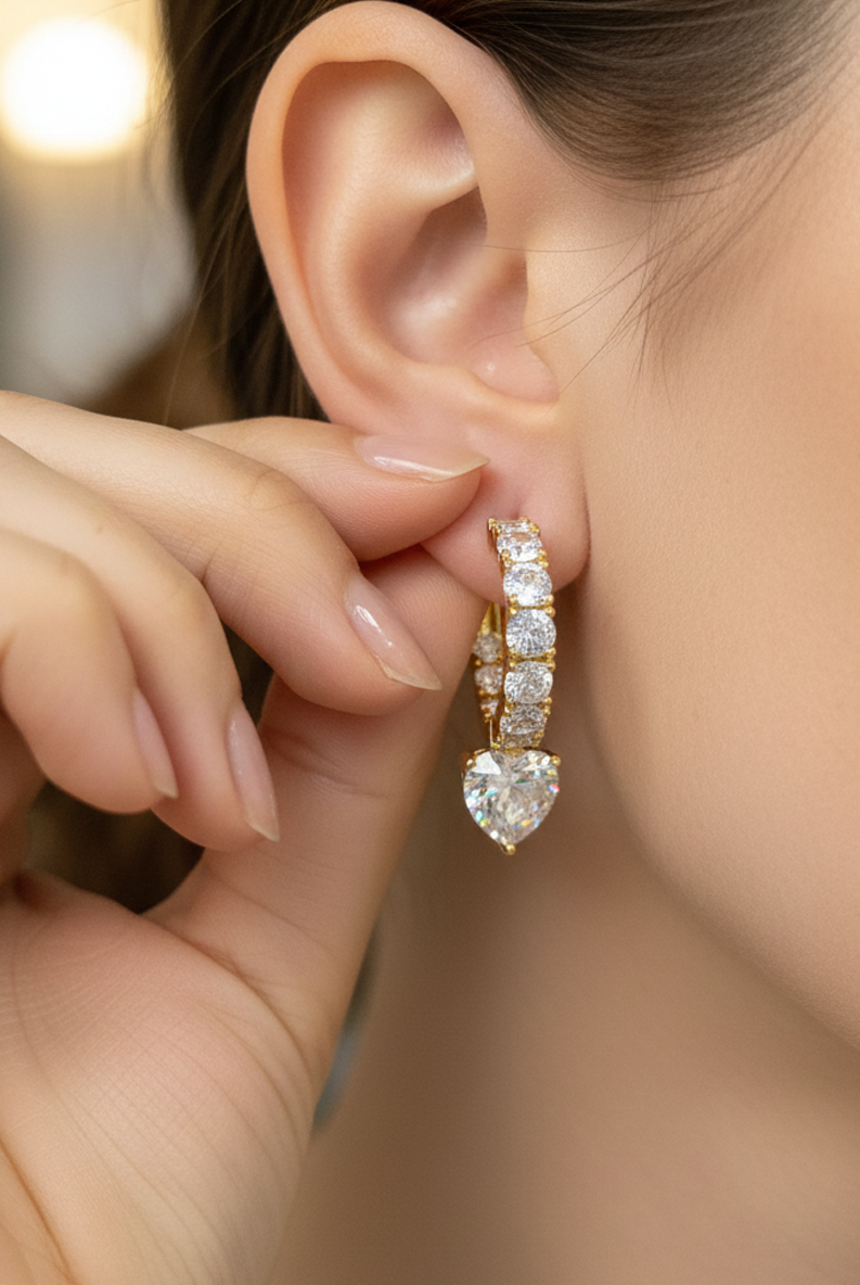 Gold-tone huggie hoop earring with dangling pavé heart charm, on ear