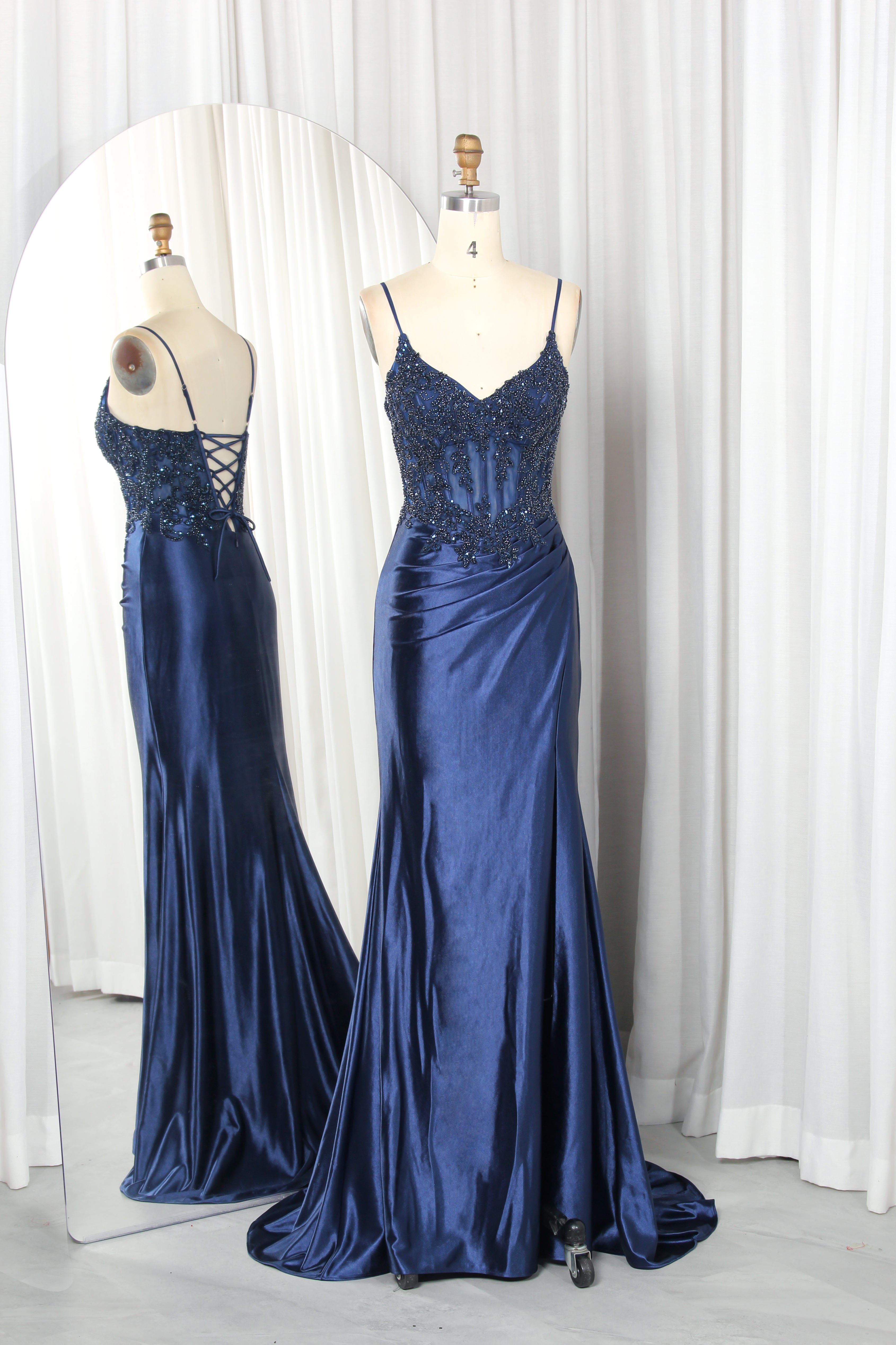 Front and back view of a navy blue evening gown featuring a sequined lace corset bodice with spaghetti straps and a draped satin skirt with a high slit.