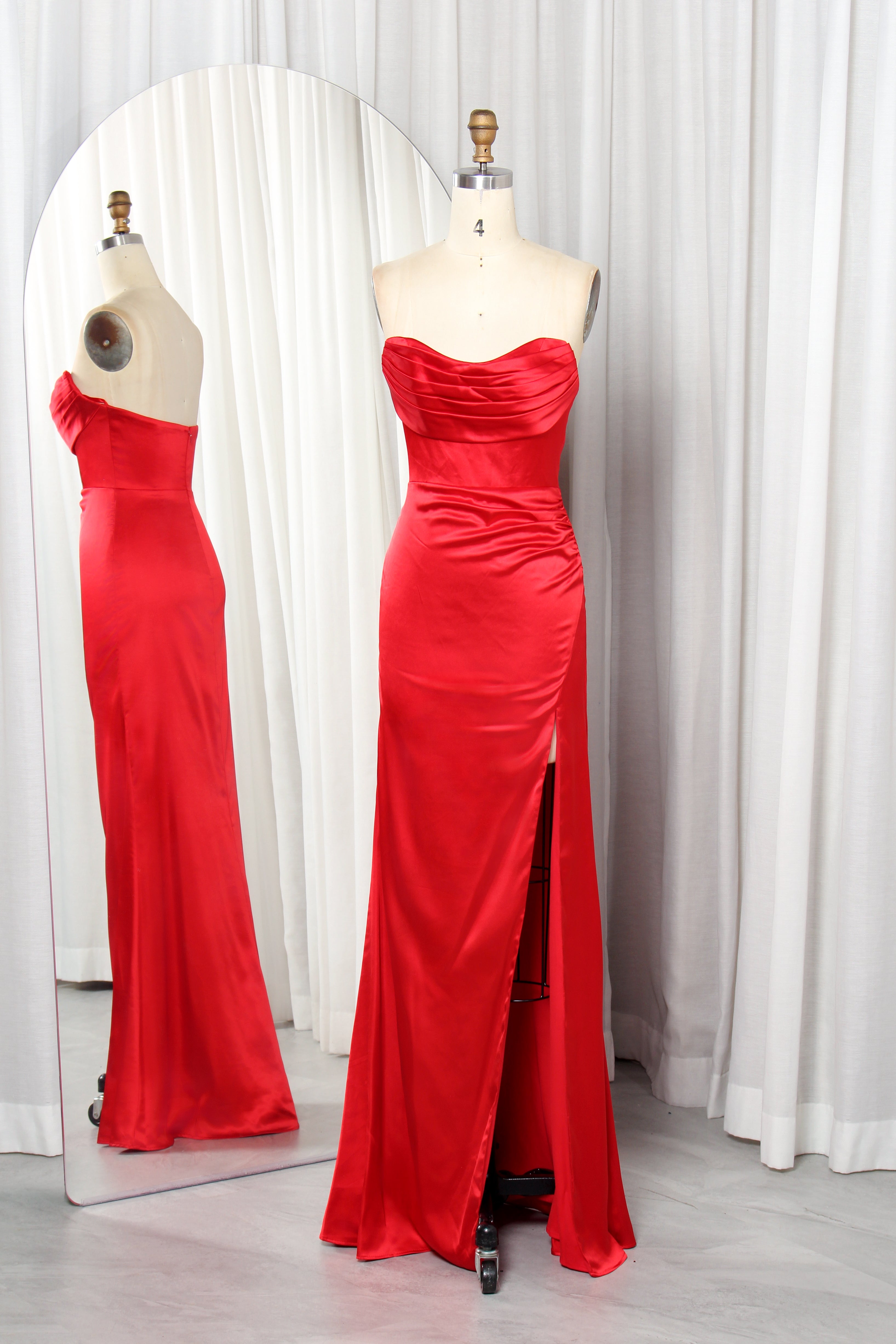 Front and back view of a vibrant red strapless satin evening gown with a ruched sweetheart neckline and high leg slit on a mannequin.