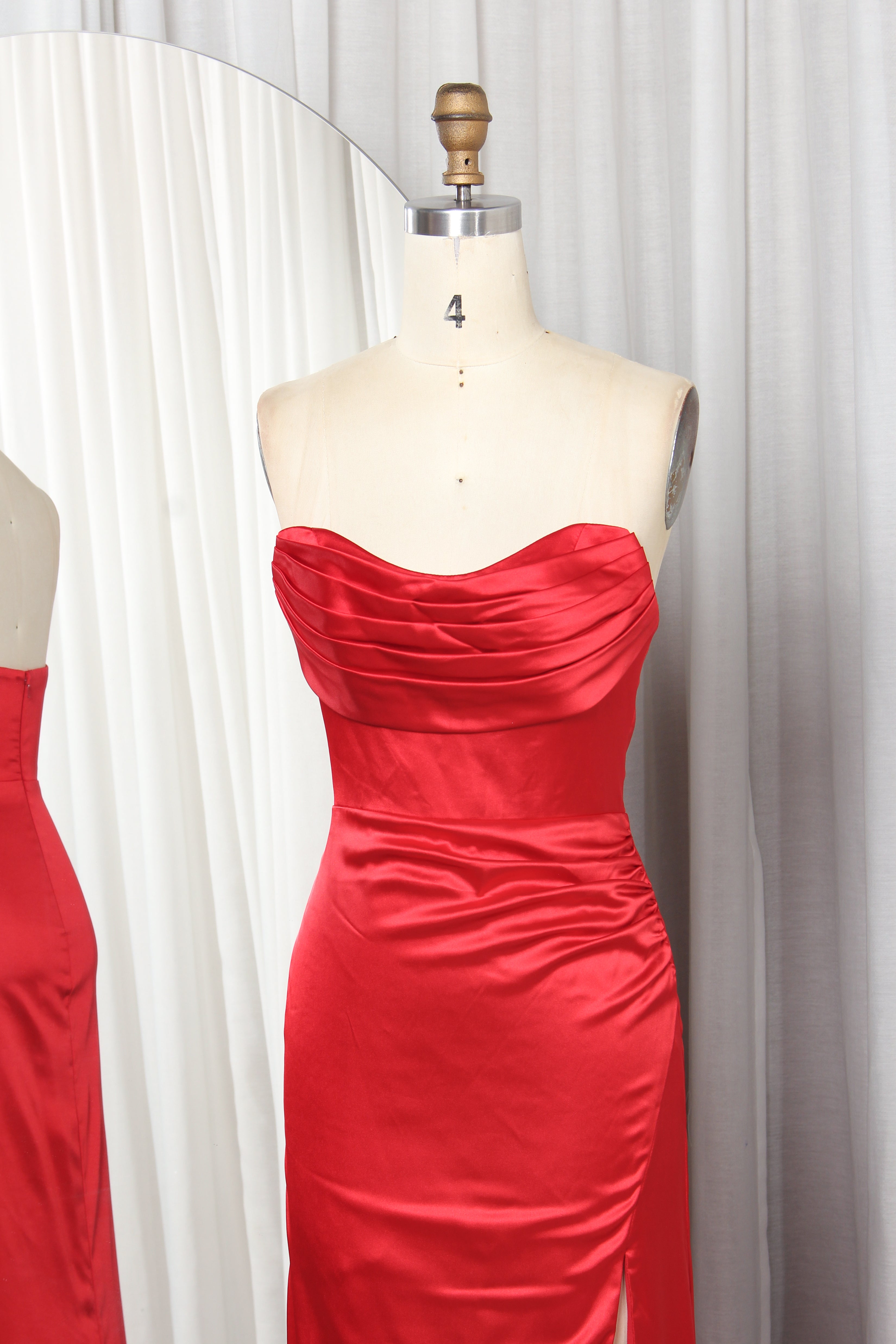 Front and back view of a vibrant red strapless satin evening gown with a ruched sweetheart neckline and high leg slit on a mannequin.