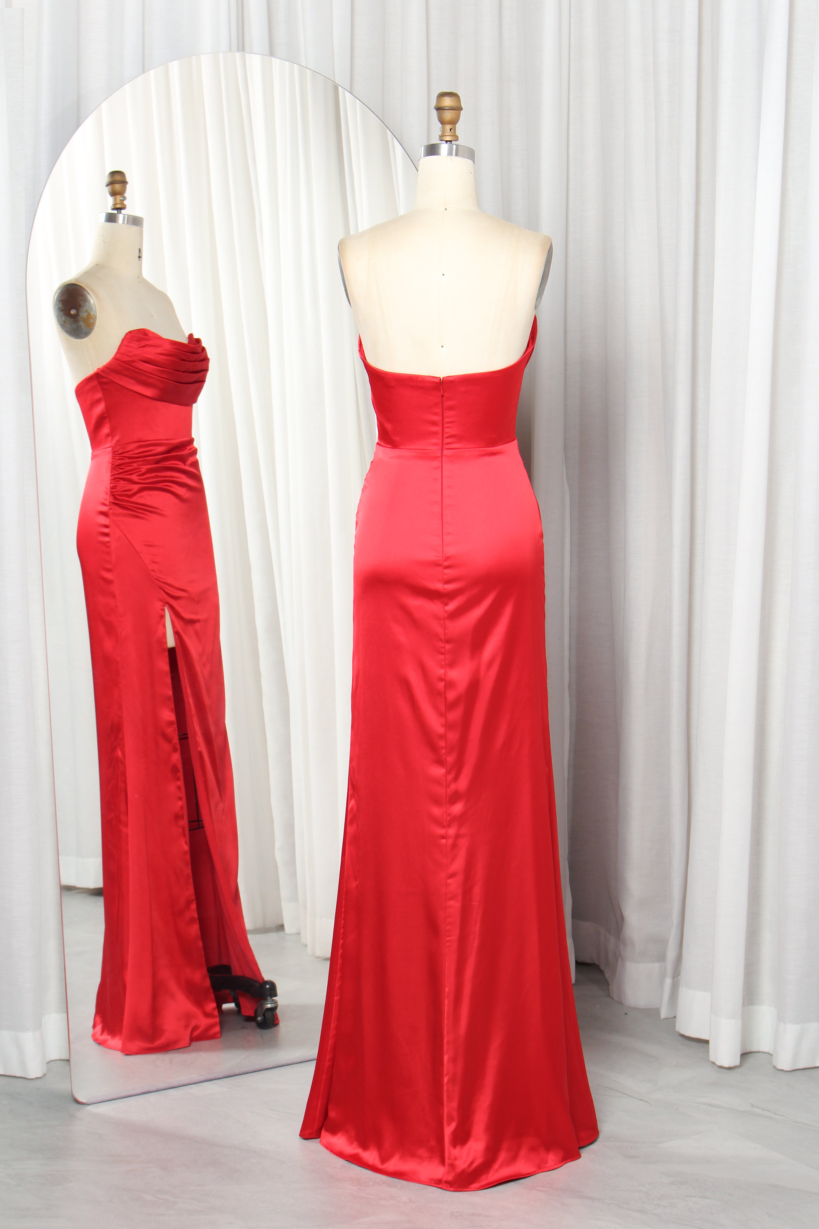 Front and back view of a vibrant red strapless satin evening gown with a ruched sweetheart neckline and high leg slit on a mannequin.