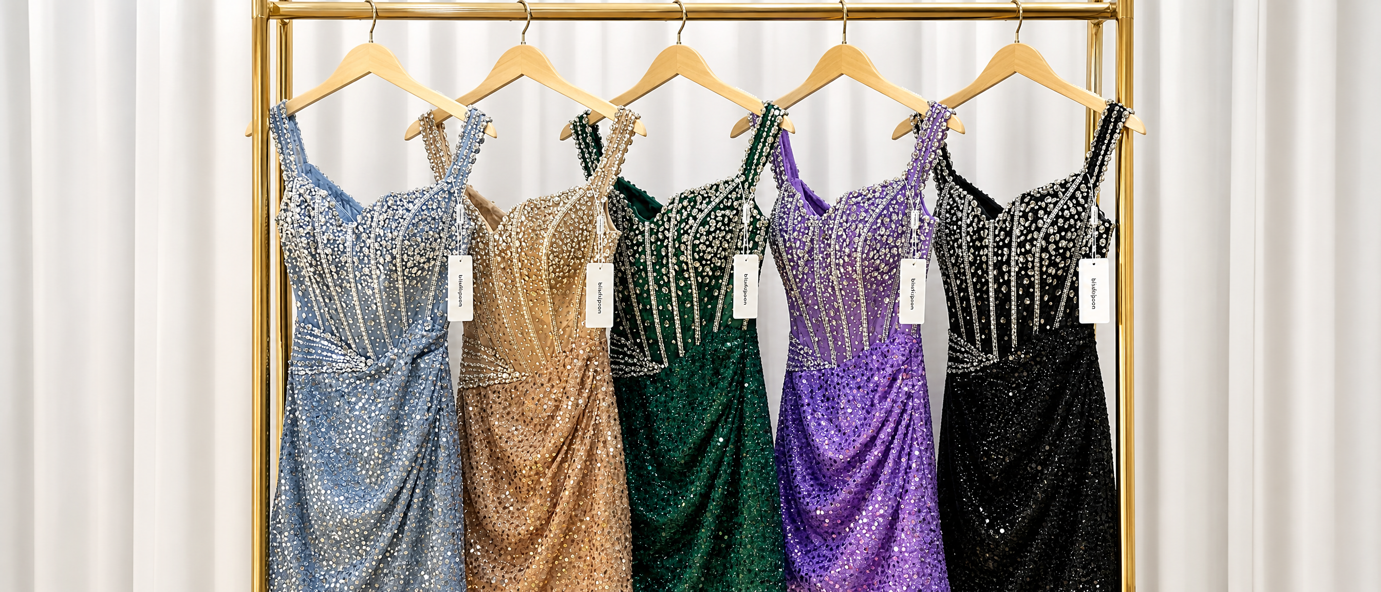 Five heavily embellished sequin mini dresses with rhinestone corset bodices hanging on a gold clothing rack. The colors from left to right are dusty blue, champagne gold, emerald green, lavender purple, and classic black.