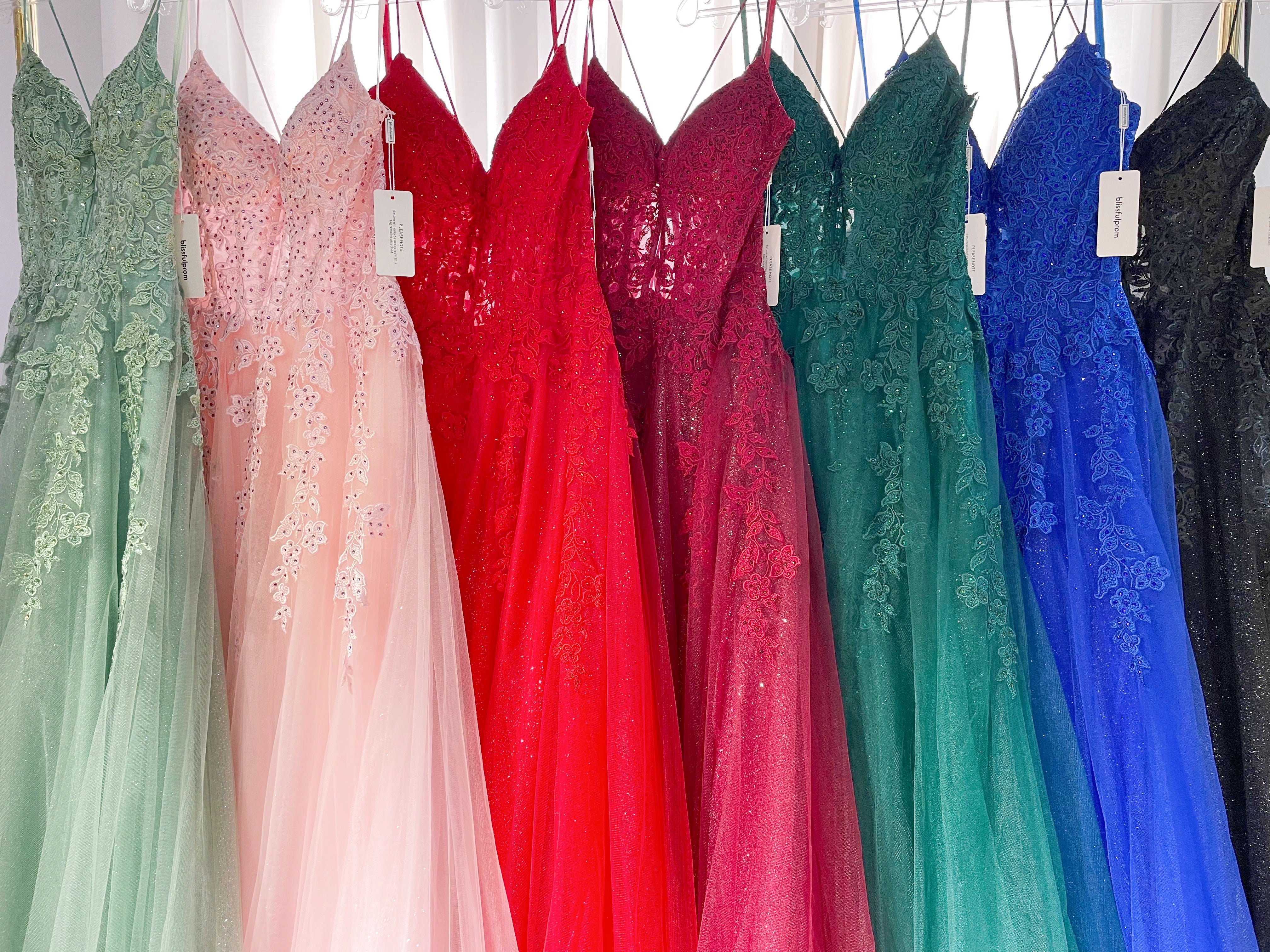 Colorful prom dresses hanging on a rack, featuring green, red, pink, and black styles