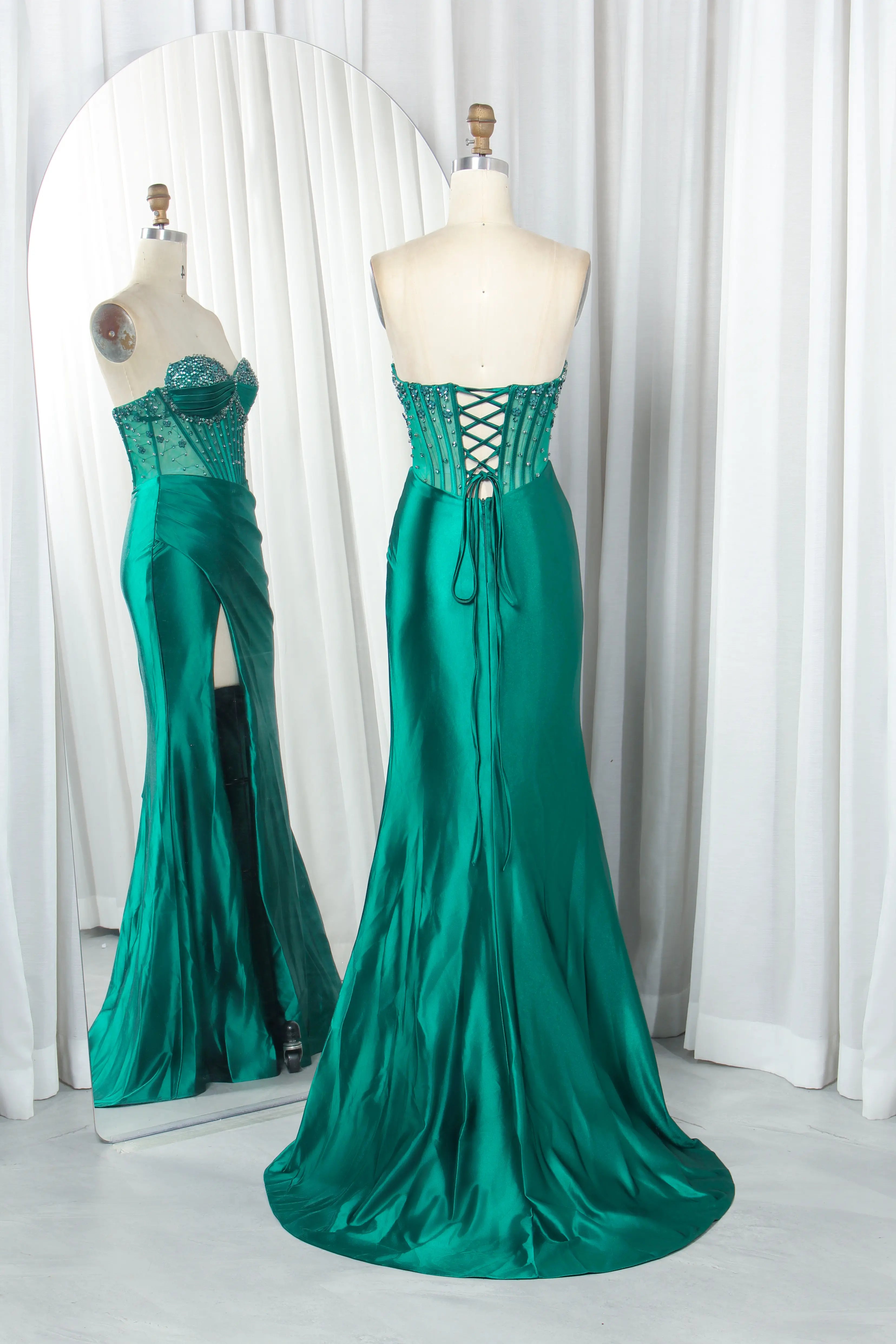 Emerald green prom dress on mannequins: corset back crisscross lacing, slit skirt