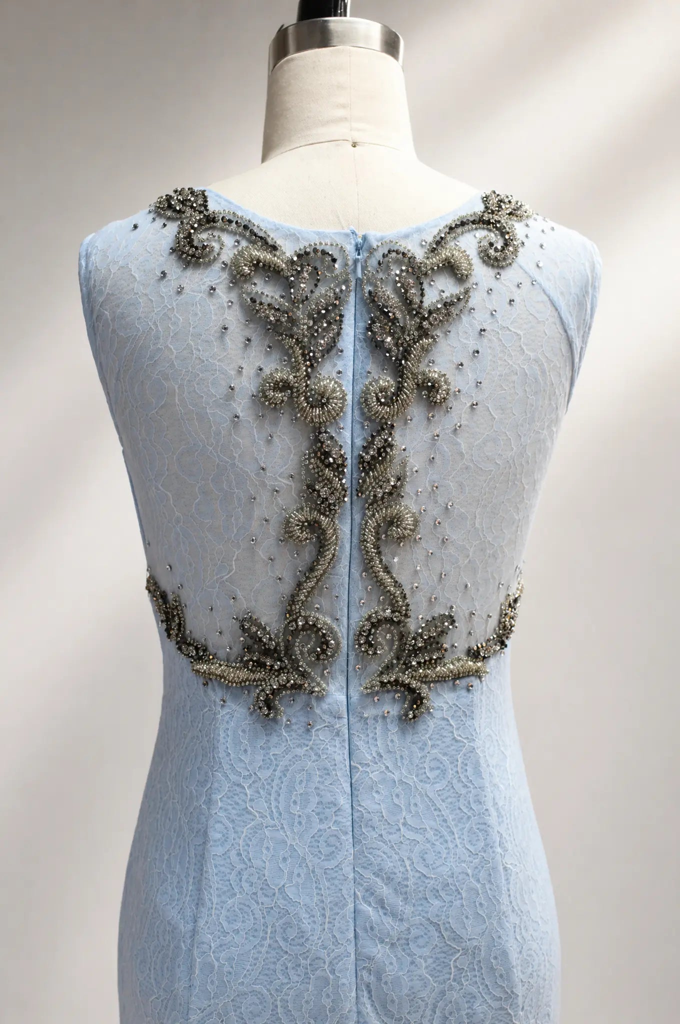 Sky blue lace appliqué gown with ornate beaded open-back design on mannequin